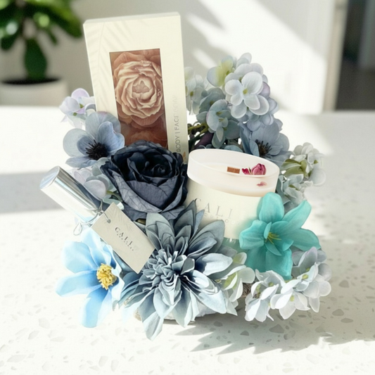 blue floral gift basket with shades of blue flowers with products in it on a white surface
