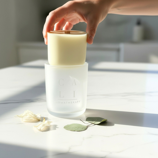 Hand holding a cylindrical candle refill with a wooden wick on a white surface with Cali Love branding.