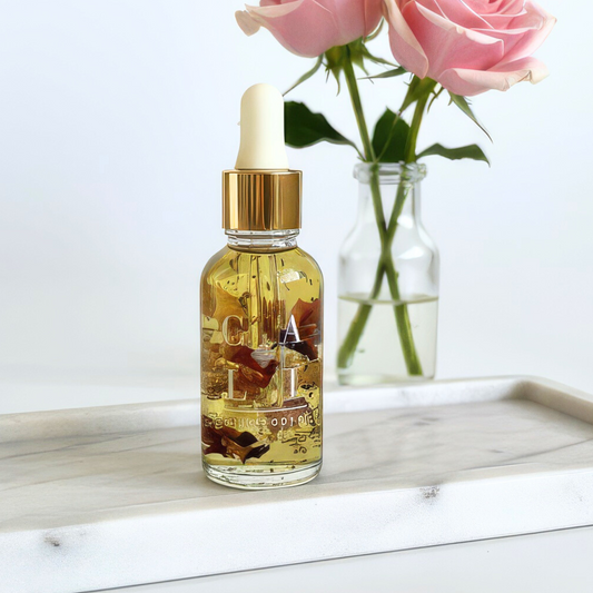 Glass dropper bottle with gold cap made with dried rose petals and 24k gold on a marble surface with pink roses in the background