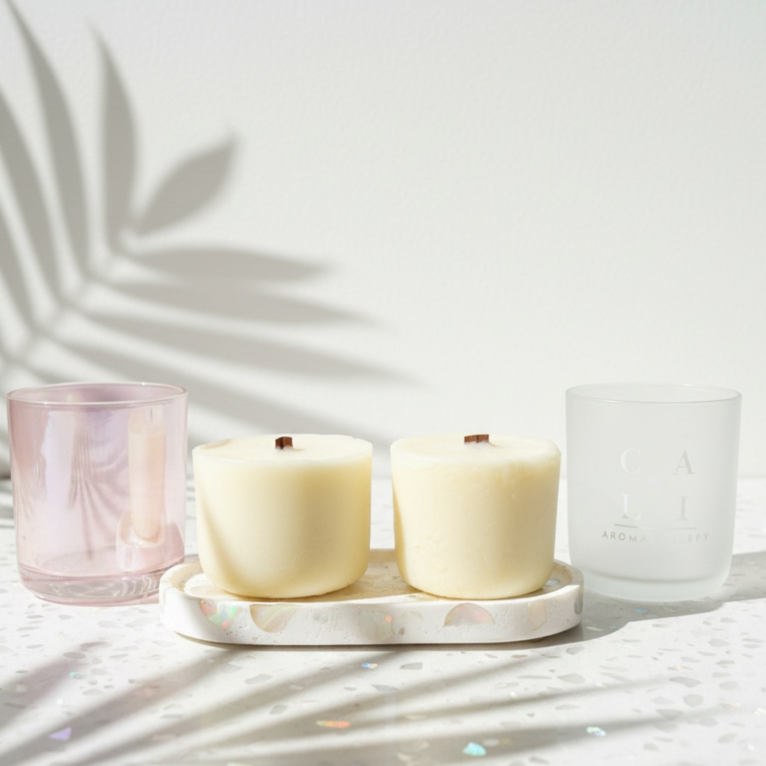 Two candle jars and two candle refills on a marble tray with two glasses, one pink and one clear, on a light background.