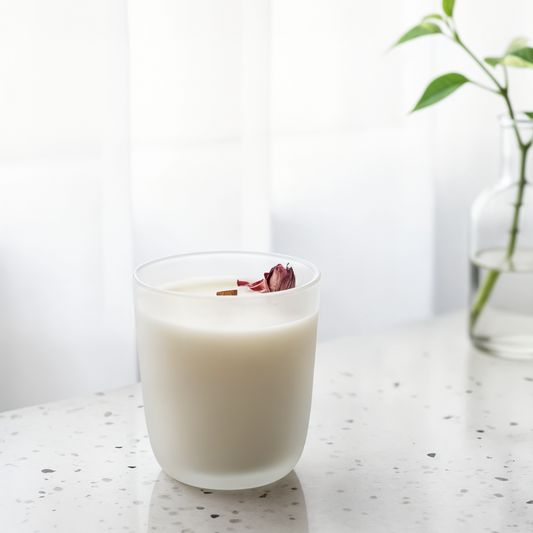 cali dream candle in a white frosted glass with a pink rose on top with a light blurred background