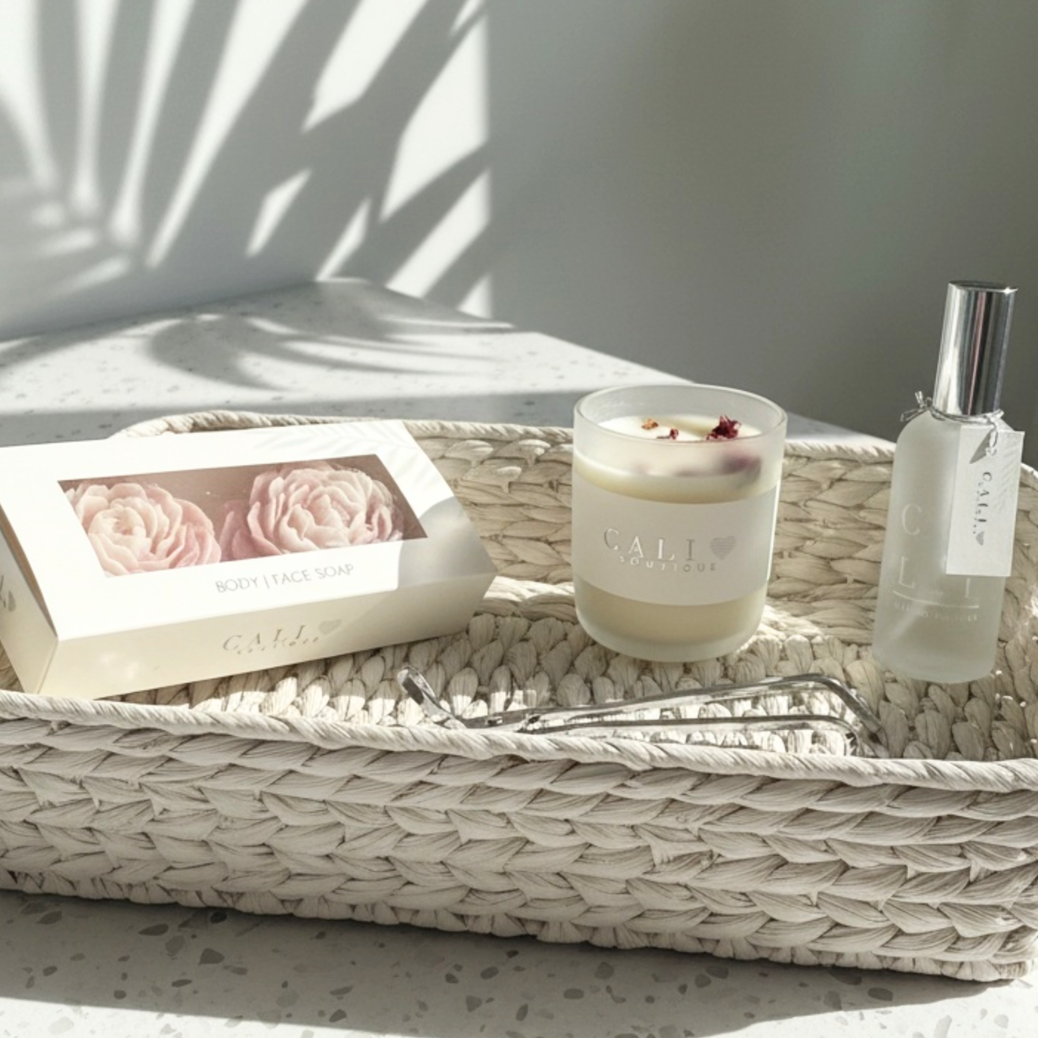 frosted glass candle and spray bottle with peony shaped soaps in linen packaging and a silver wick trimmer in a basket