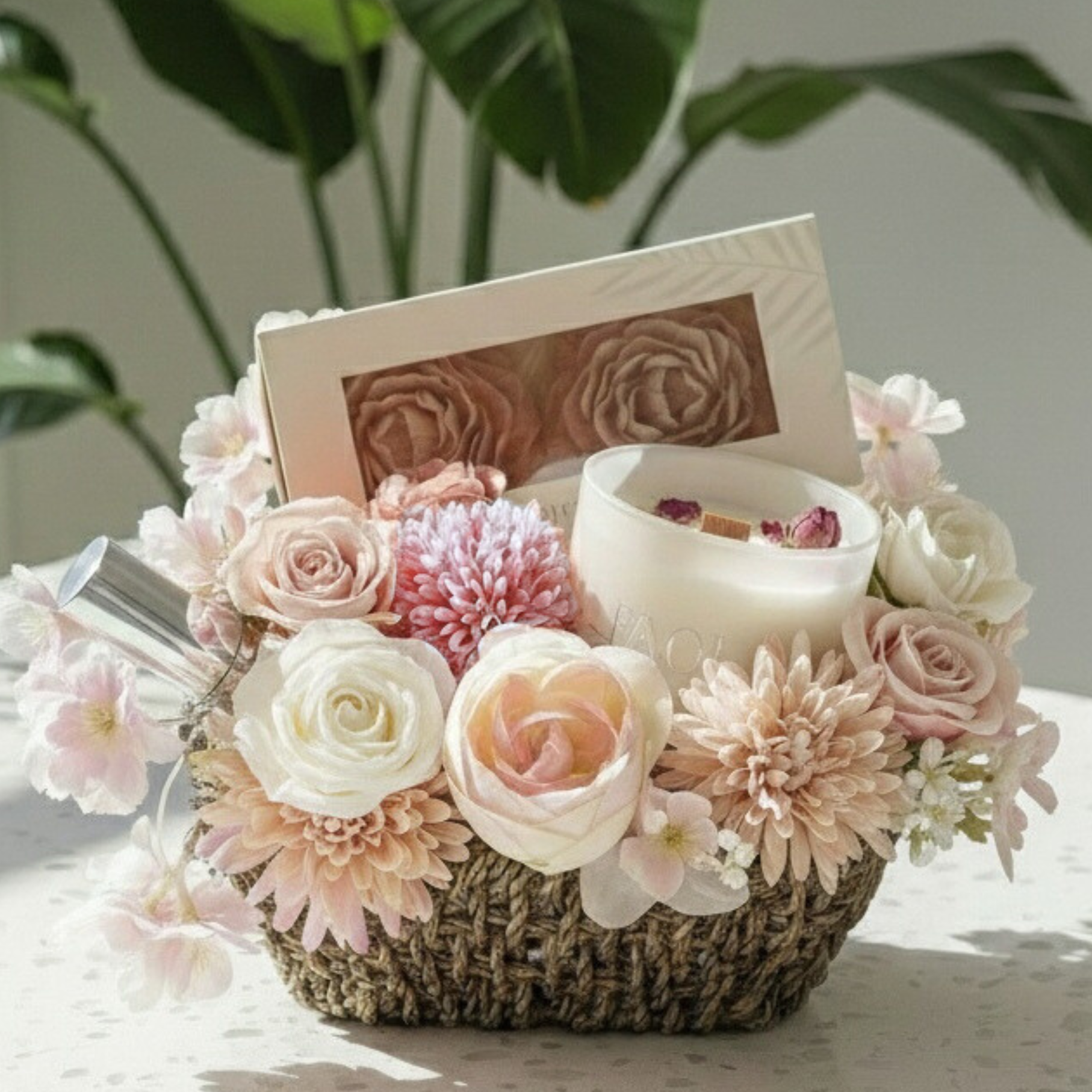 Decorative basket with flowers, a candle, and a set of soaps in linen packaging on a light surface.