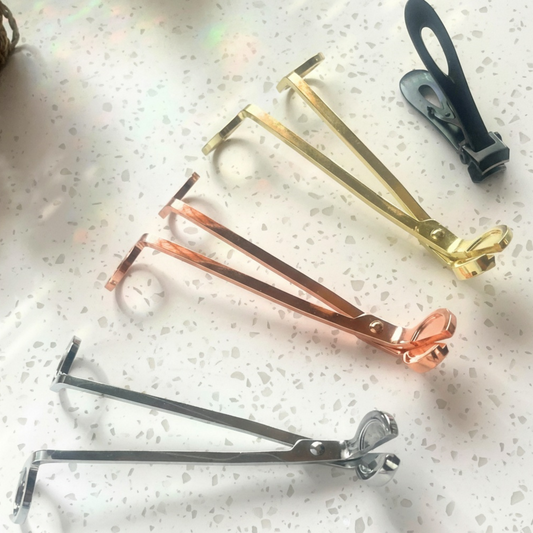Set of candle wick trimmers in gold, rose gold, and silver or black on a speckled surface.