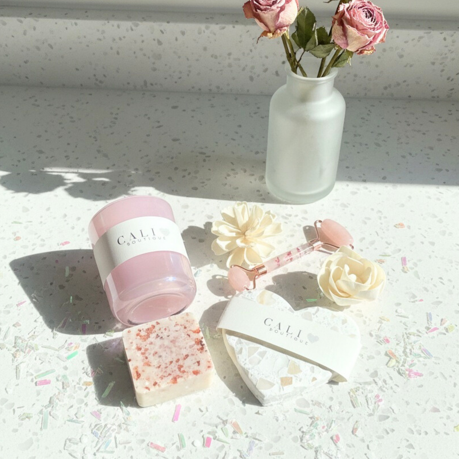An iridescent pink candle, salt soap, and decorative flowers on a textured surface with Cali Love Boutique branding.