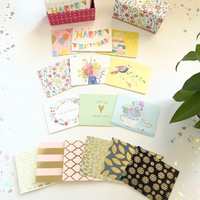 Collection of various patterned greeting cards on a light surface with a plant in the corner.