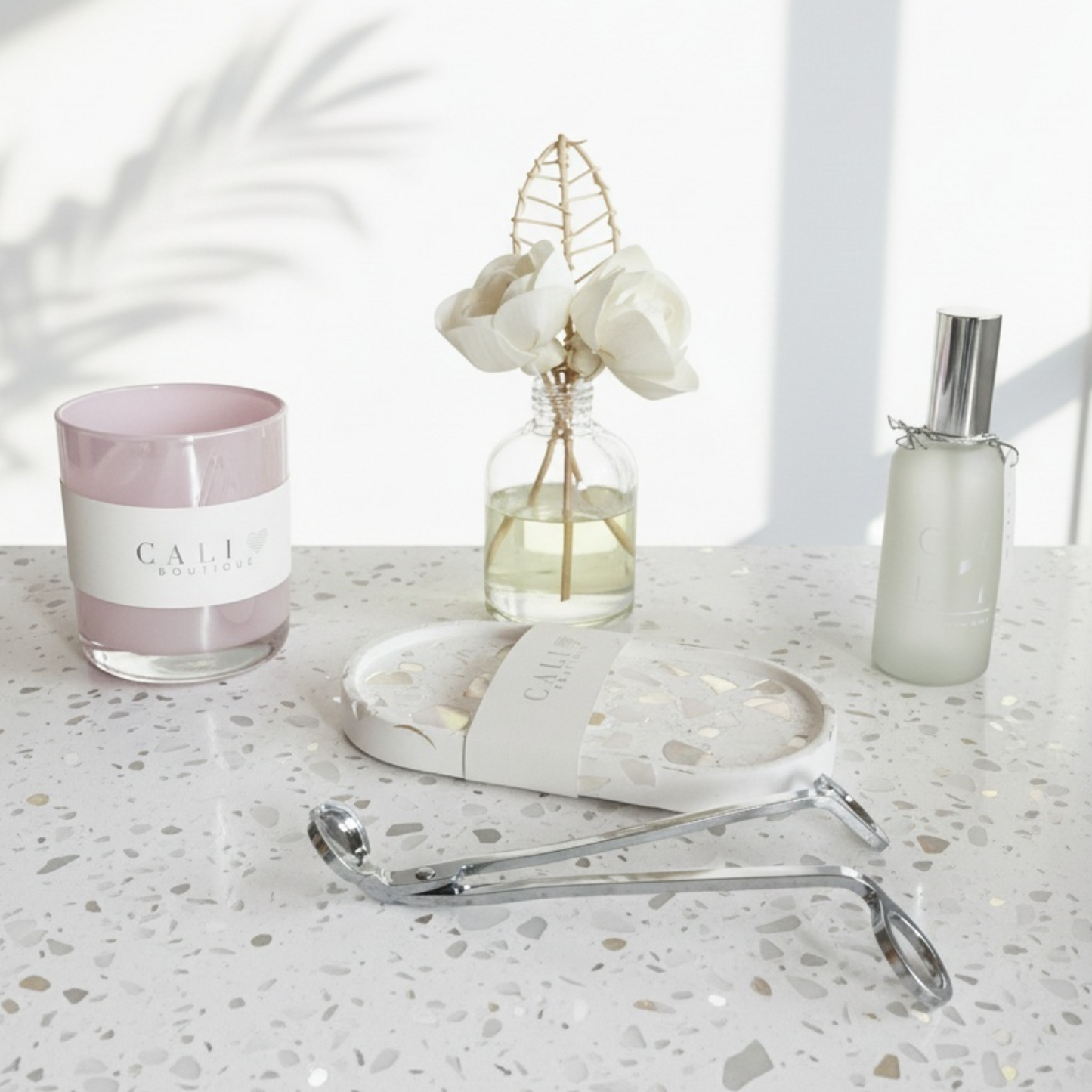 Candle, reed diffuser, mood mist, trinket tray and wick trimmer on a light surface
