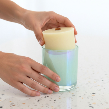 Hand holding a candle with a glass container on a speckled countertop