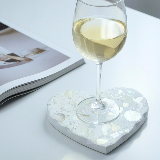 Heart-shaped stone coaster with a glass of white wine on a light surface.