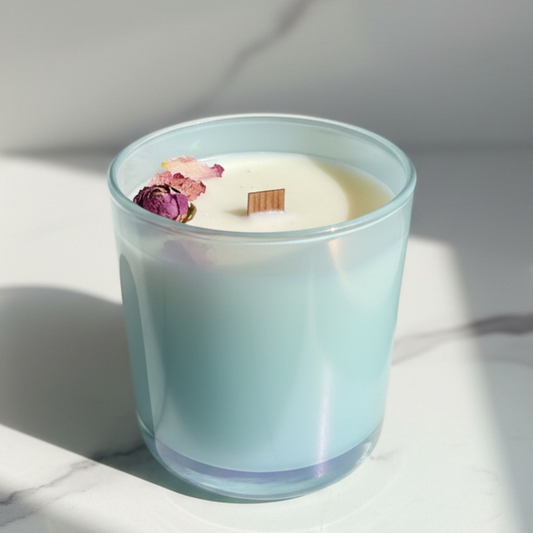Candle in a light blue glass container with dried flowers on a marble surface