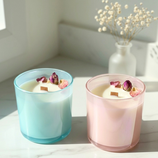 Two scented candles in blue and pink glass with floral elements on a light surface.