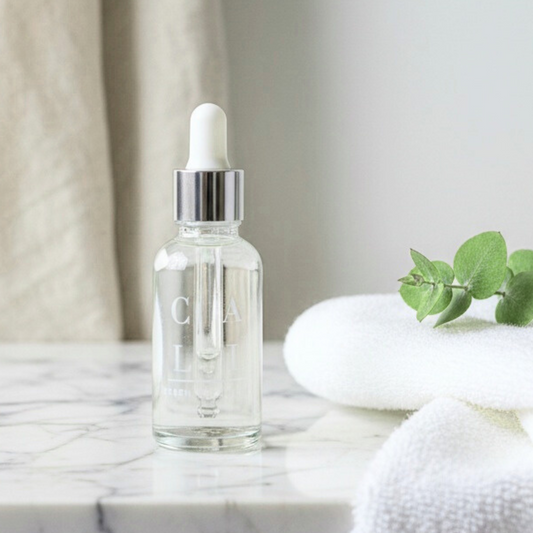 Clear glass dropper bottle with hyaluronic acid and green tea on a marble surface with towels and green leaves.