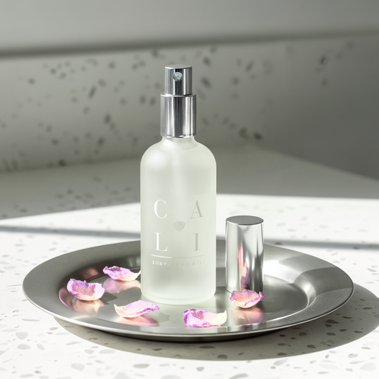 Frosted spray bottle labeled 'CALI Love Aromatherapy on a silver tray with pink petals, against a light background.